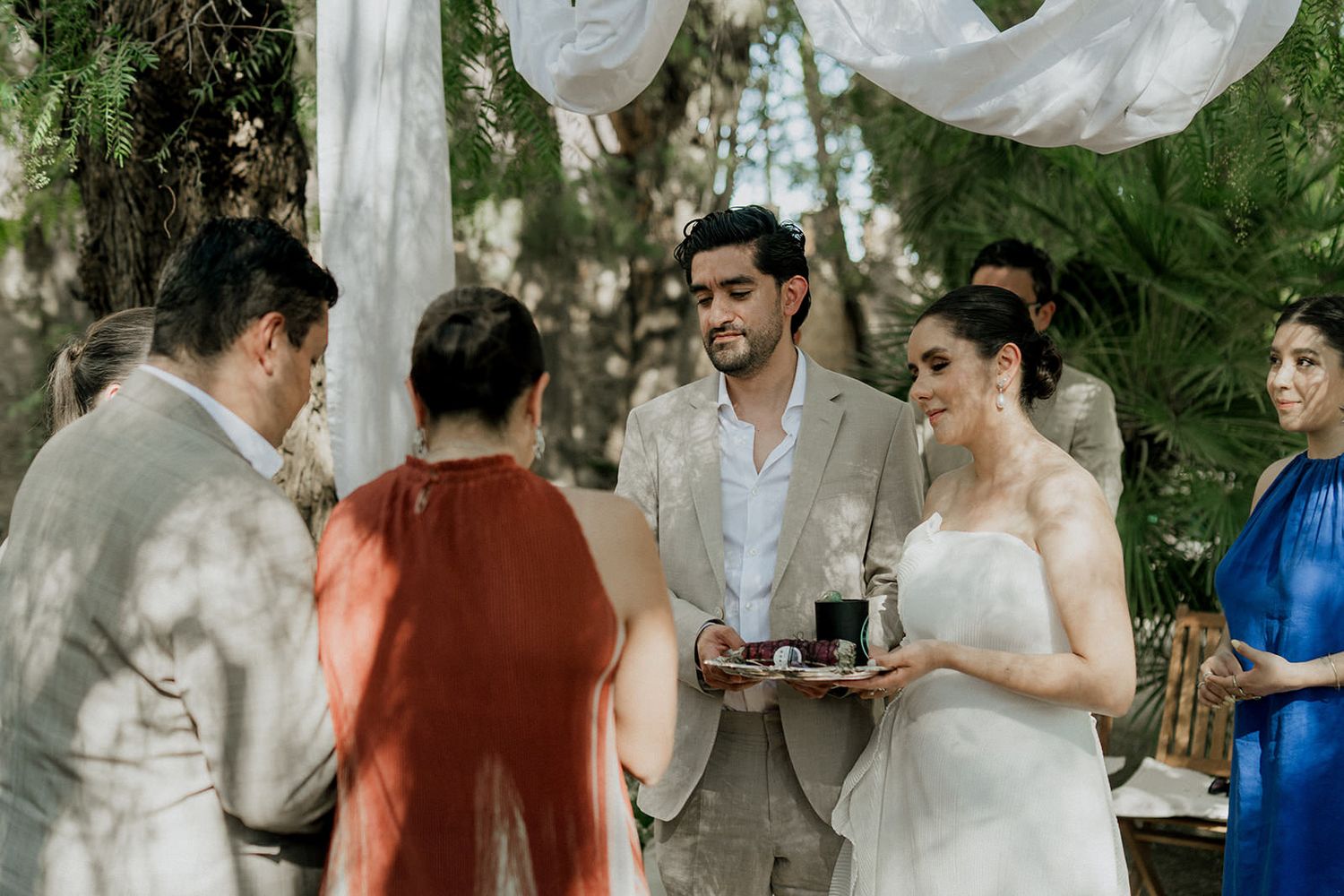 Guests mingle and socialize at an outdoor wedding reception under natural greenery.