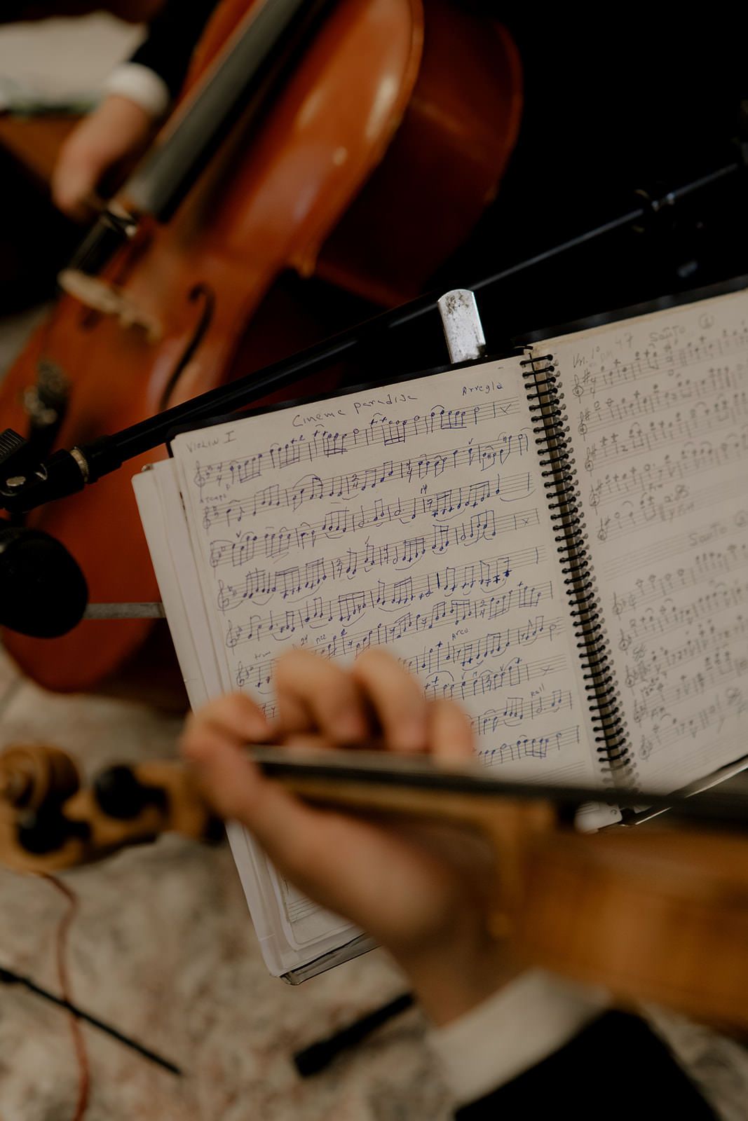 Musician reads handwritten sheet music in spiral notebook beside a violin during a recording session.