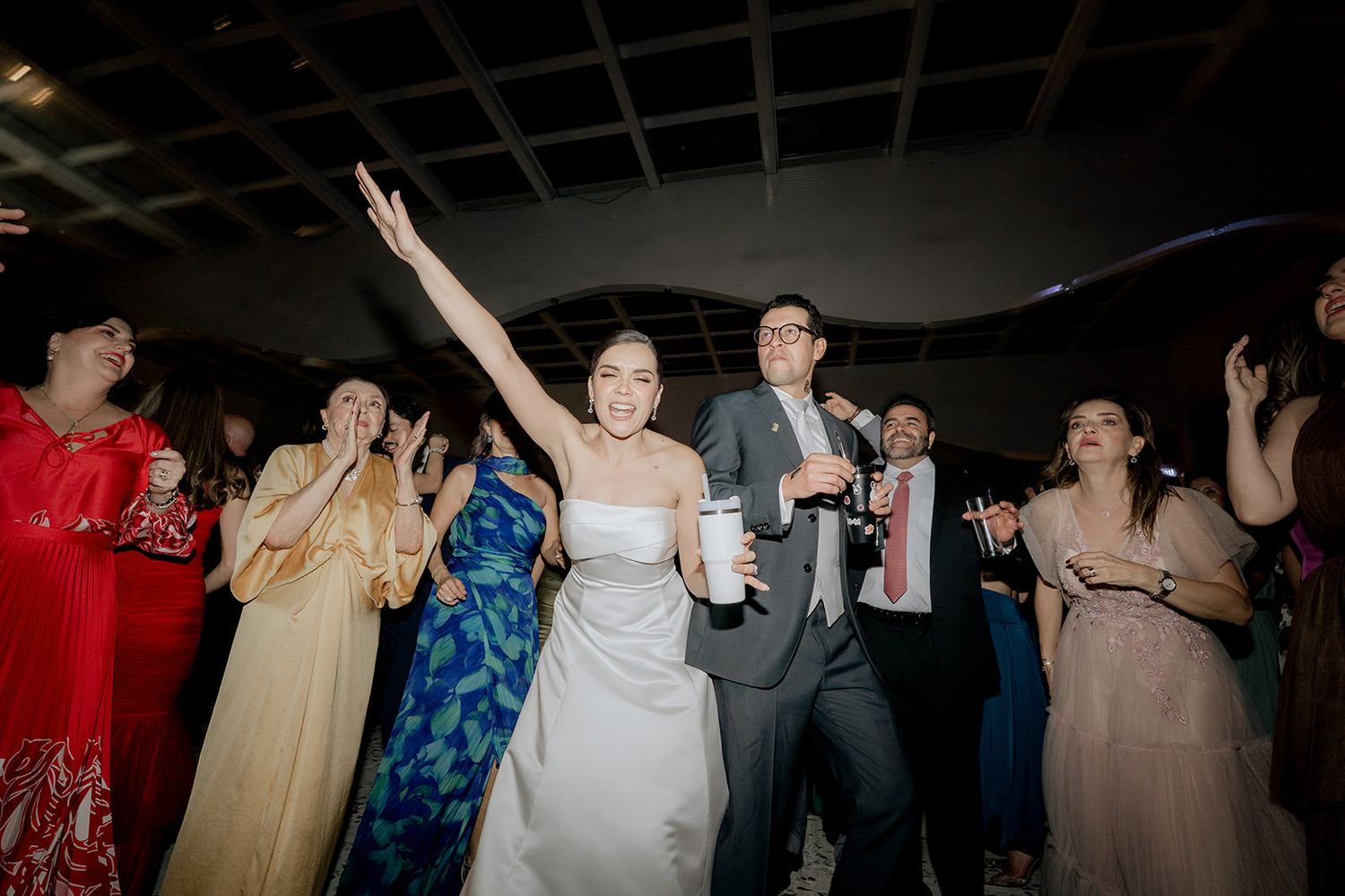 Joyful bride in white gown and groom celebrate with guests at lively wedding reception.