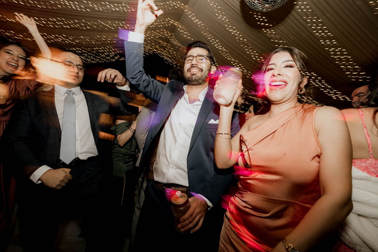 Guests dancing and celebrating under decorative lighting at wedding reception party.