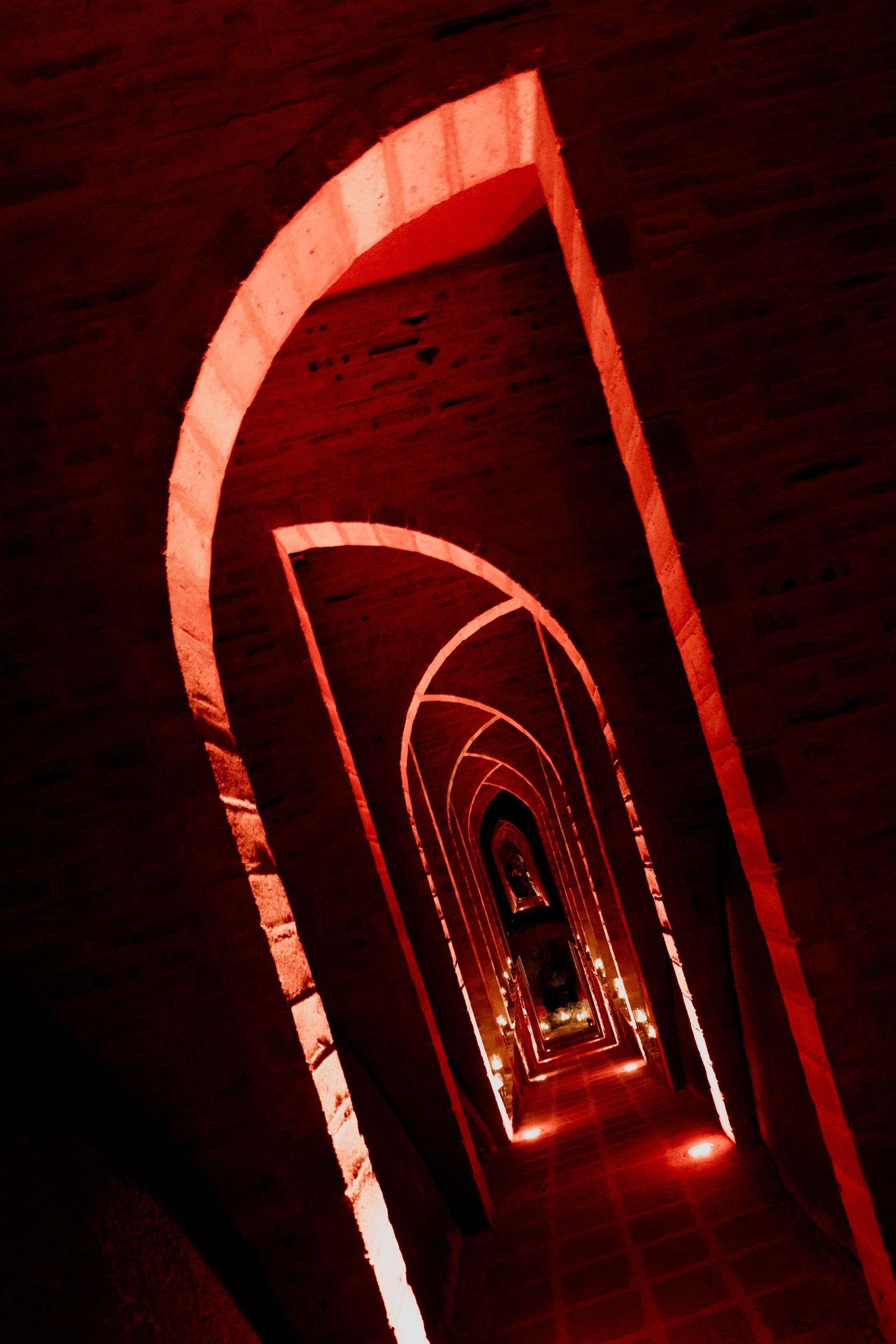Dramatic red-lit stone archway corridor creates an infinite tunnel effect.