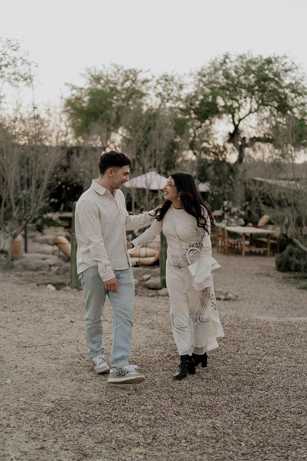 A couple shares playful moments together in a desert landscape wearing light colored outfits.