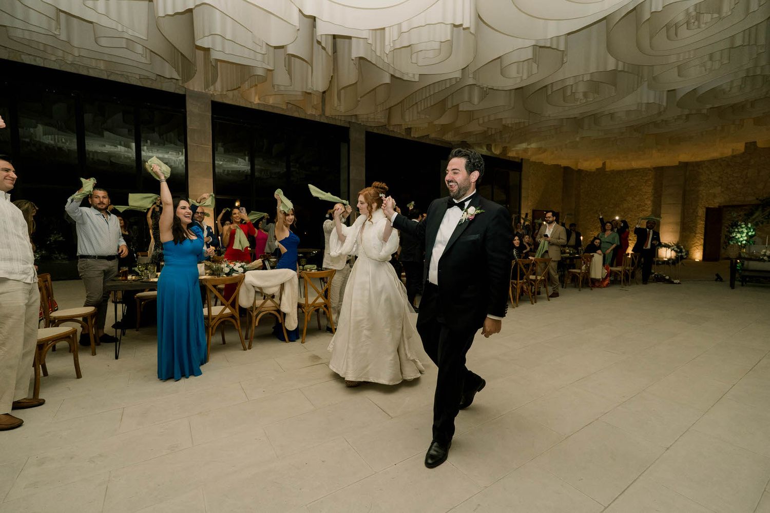 Wide angle view of wedding reception space with guests seated at tables under fabric draped ceiling.