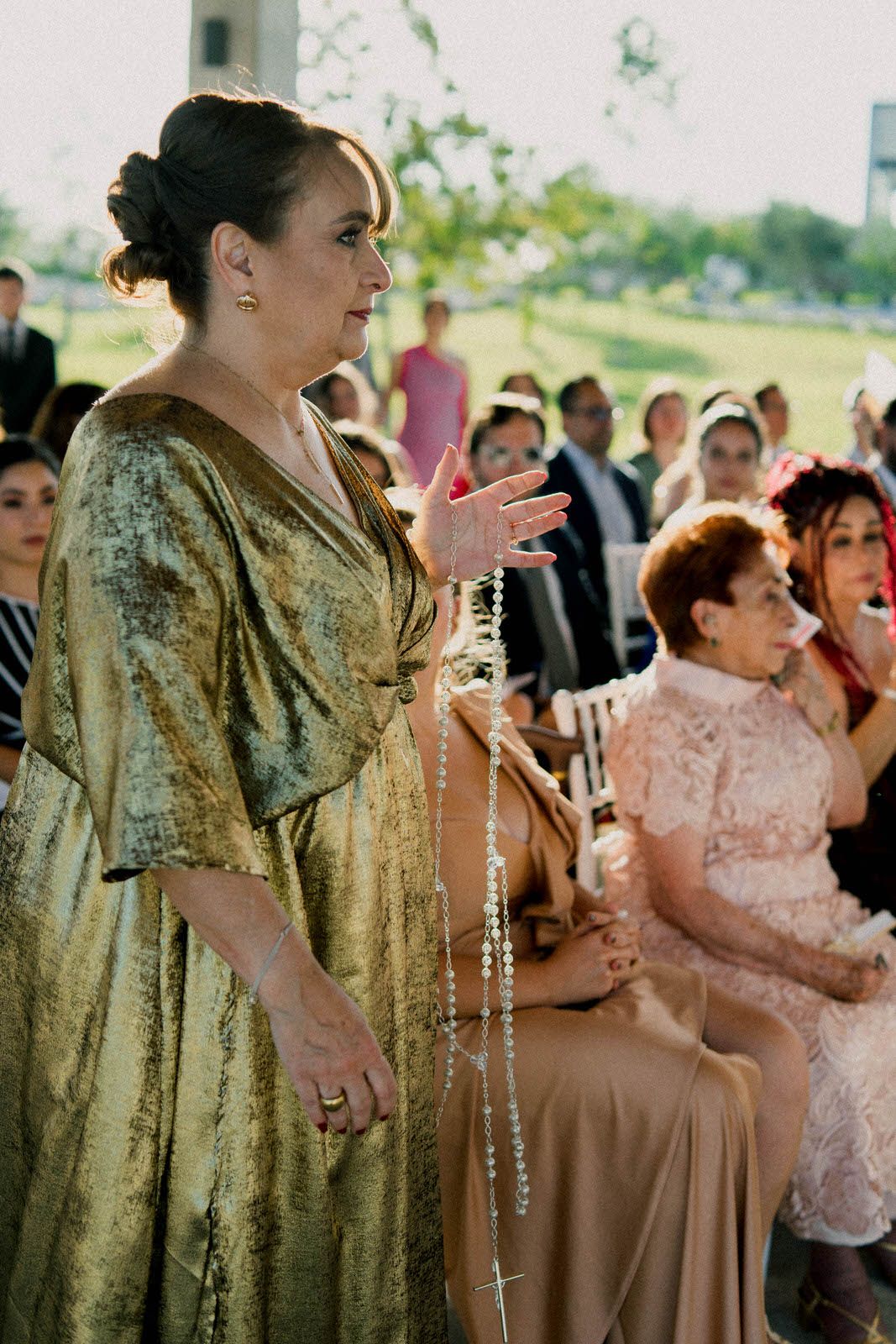 A guest in a shimmering gold dress stands during an outdoor wedding celebration.