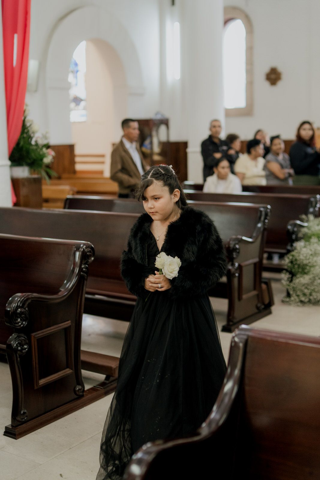 Person in black attire seated in wooden church pew during wedding ceremony.