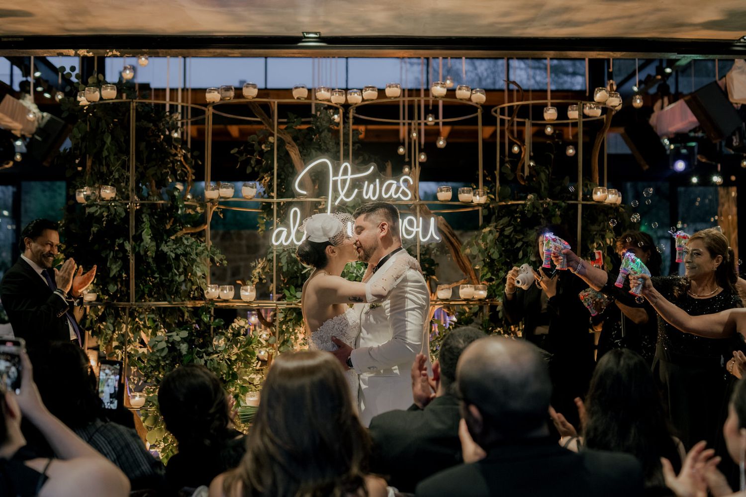 Guests celebrate a couple's first dance under a neon sign at an evening wedding reception.