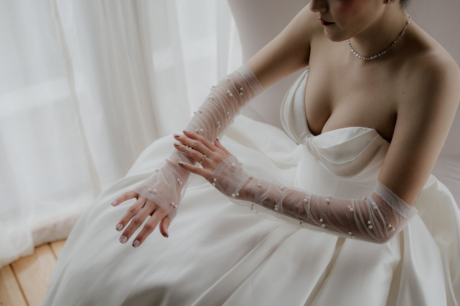Close-up of delicate tulle gloves with pearl details against a white wedding dress.