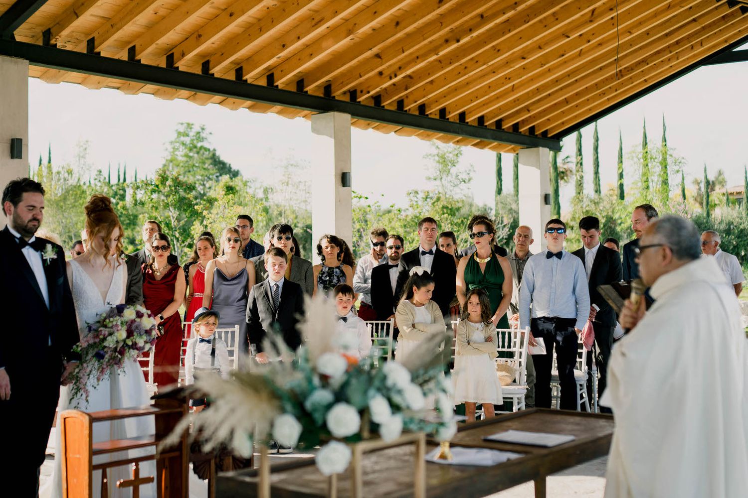 Wedding guests seated under a covered outdoor pavilion during ceremony.
