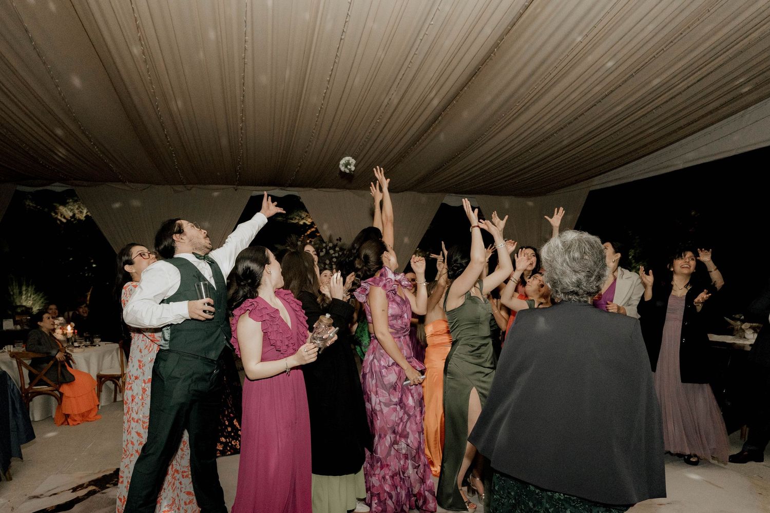 Wedding guests dance and celebrate under elegant tent with fabric ceiling draping.