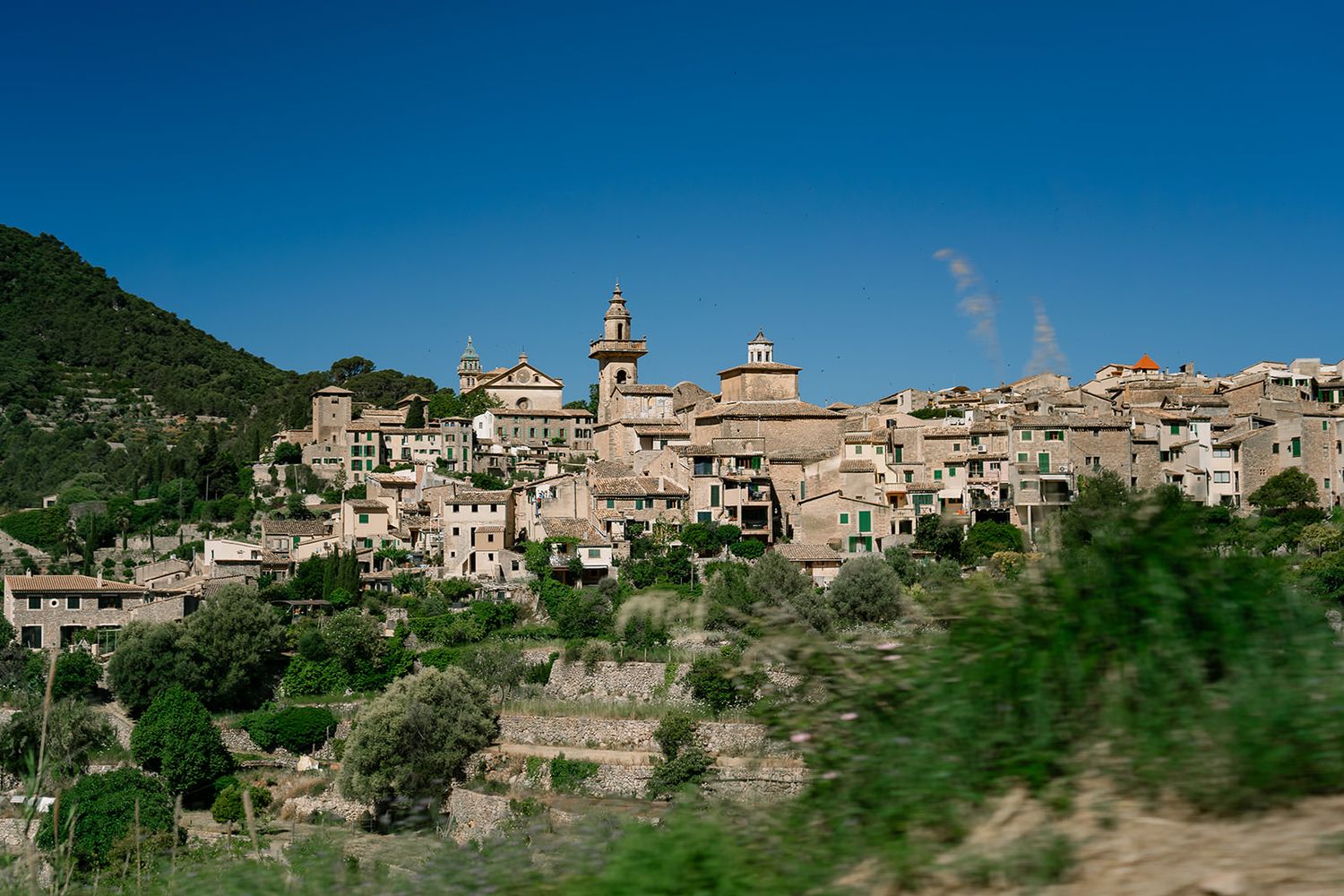 A panoramic view of a historic hilltop village with stone buildings against a bright blue sky.