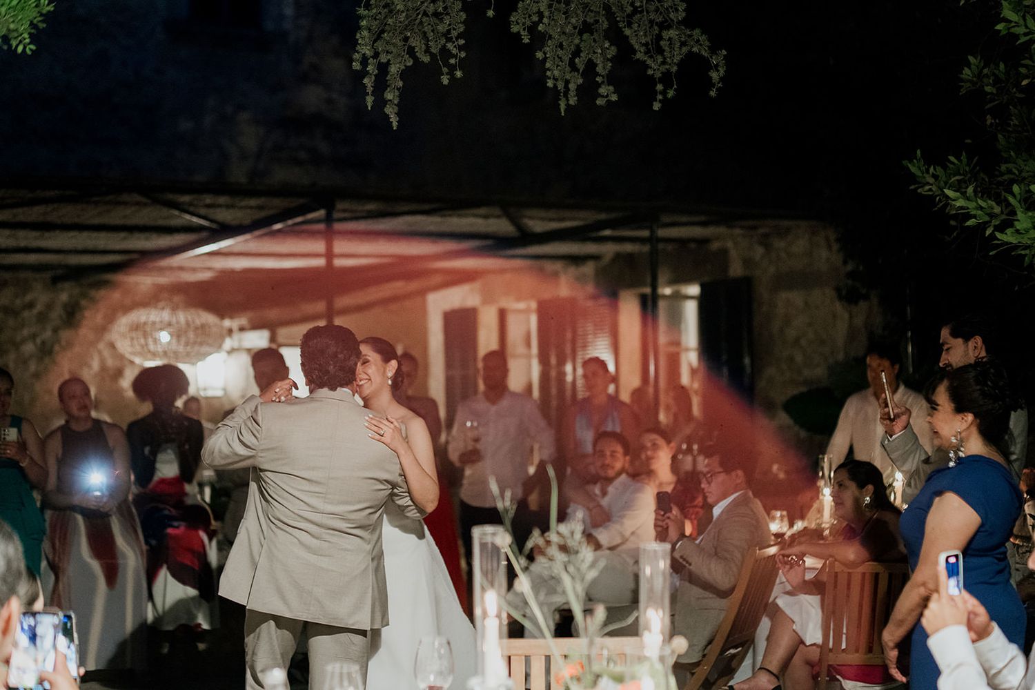 A dimly lit outdoor reception with dancing silhouettes and string lights creating an atmospheric scene.