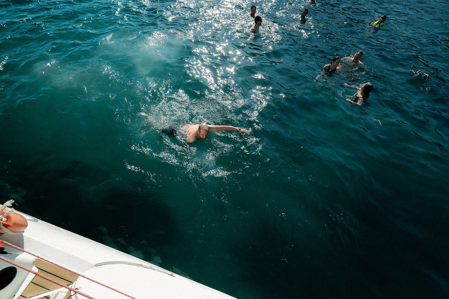 Swimmers enjoying the deep blue waters beside a sailboat on a bright day.