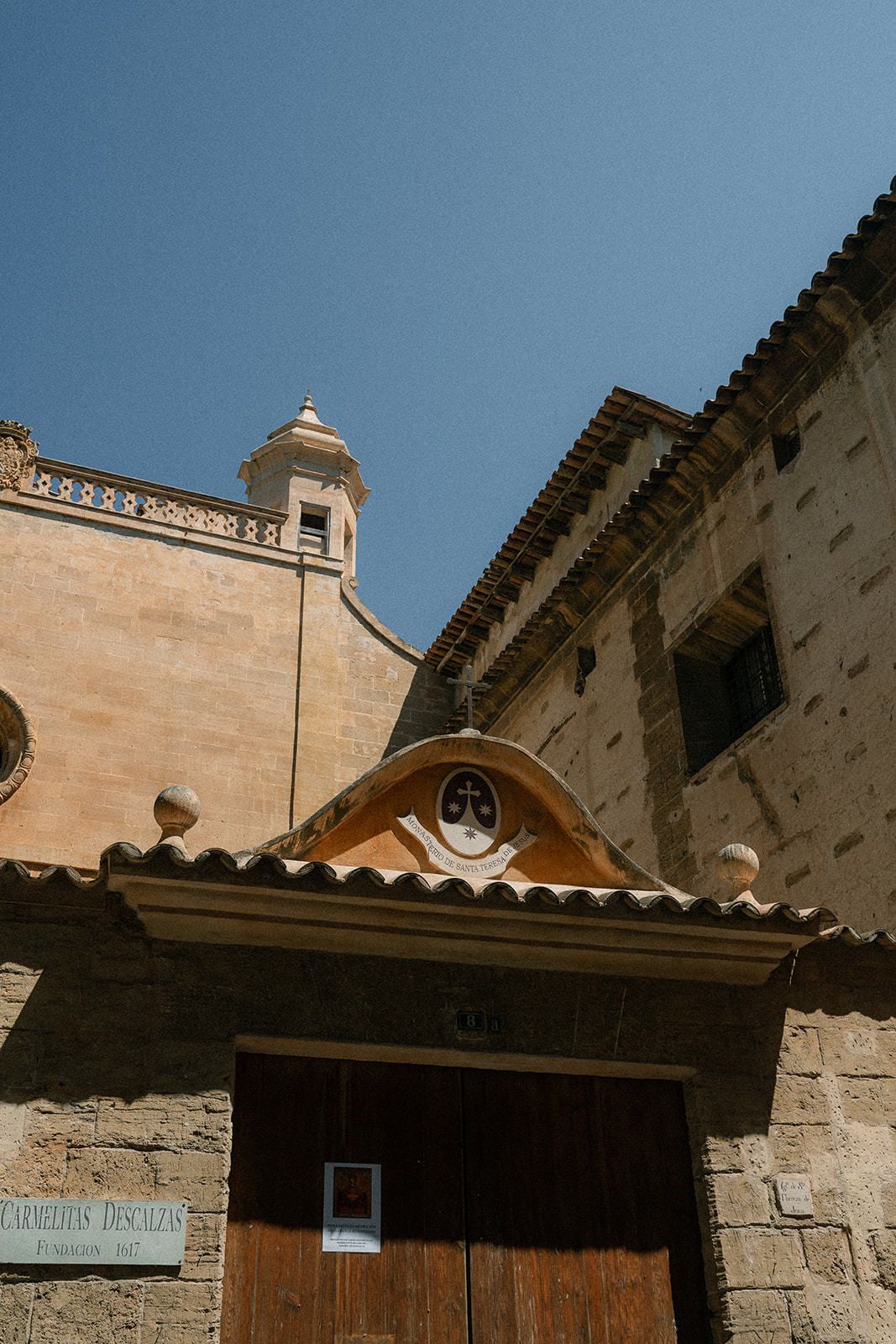 Ancient stone church facade with terracotta roof tiles and ornate architectural details against blue sky.