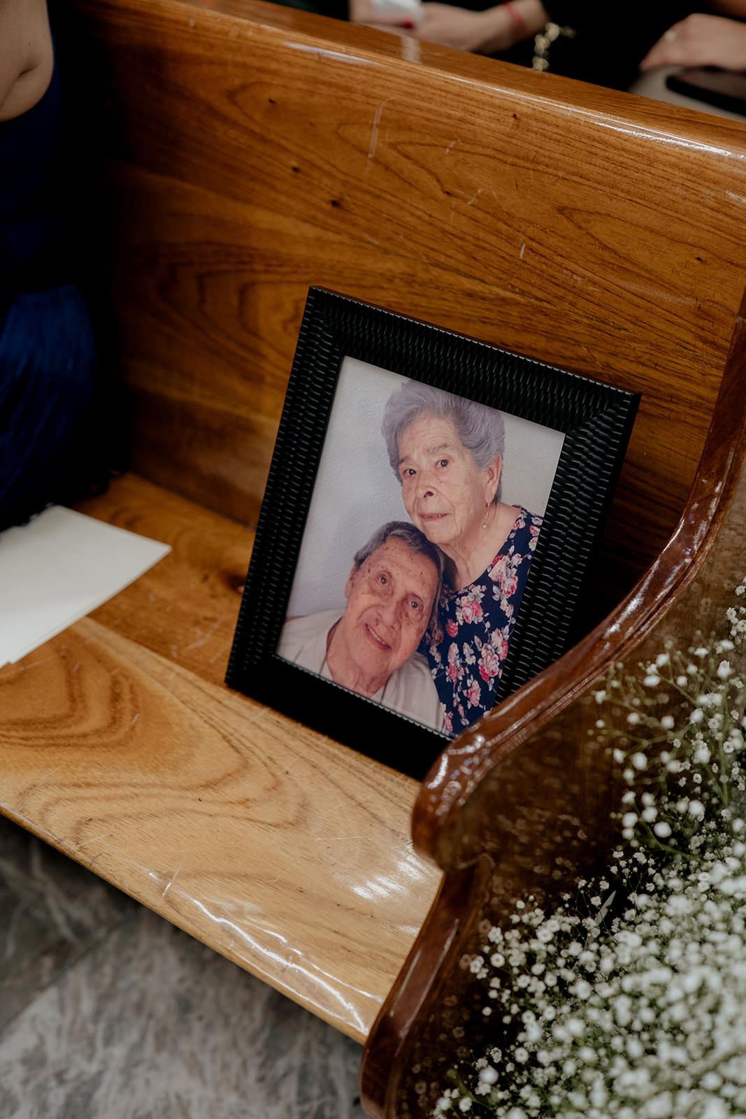 Framed photo of elderly couple displayed on church pew with baby's breath flowers at wedding.