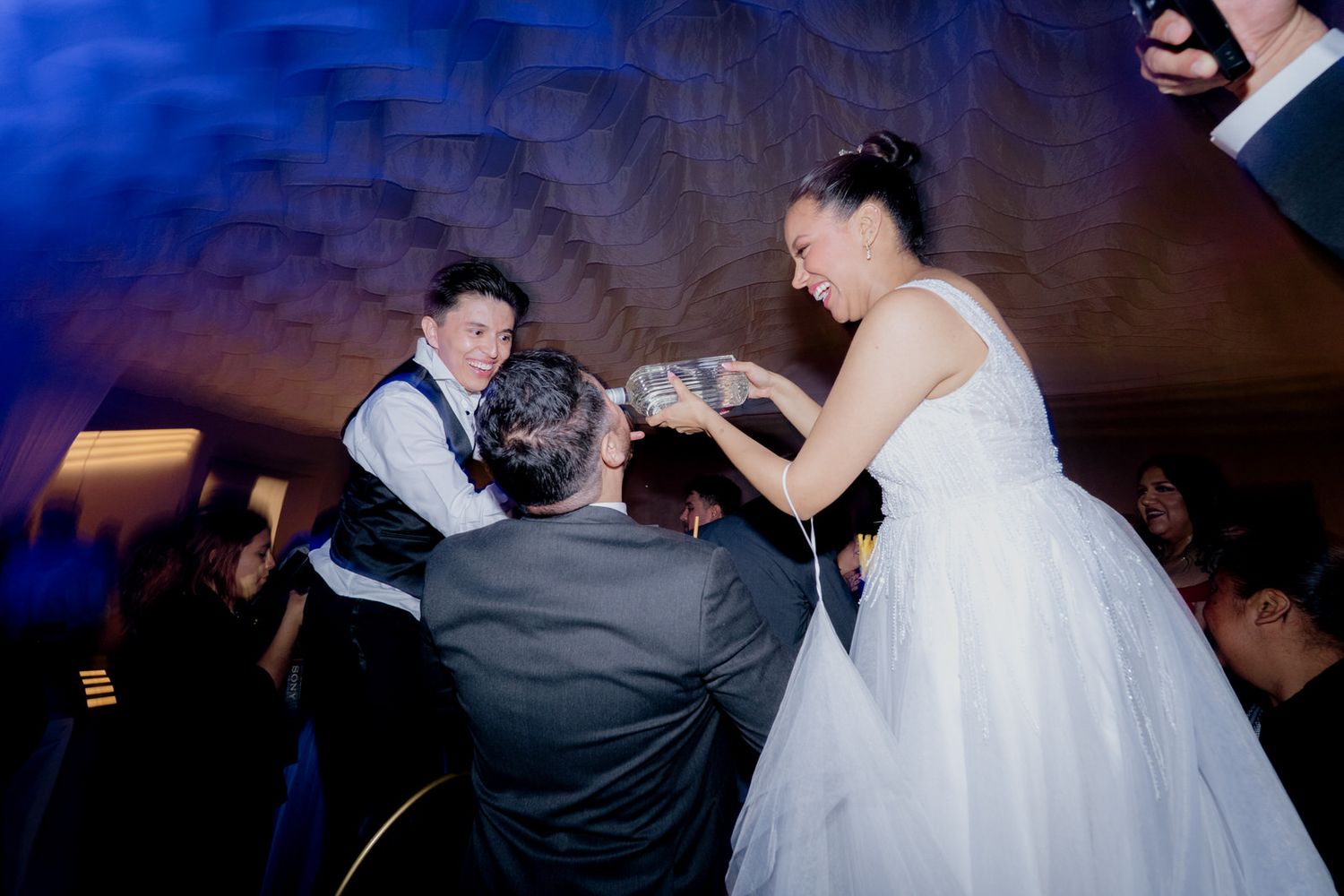 Bride in white dress celebrating with guests at a lively wedding reception party.