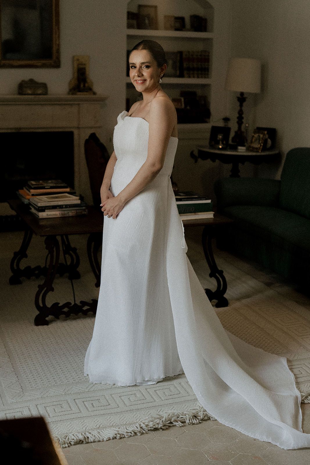 Elegant white wedding dress with flowing train photographed in a dimly lit interior setting.