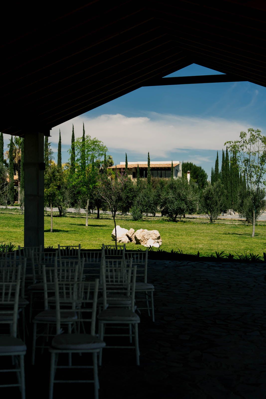 View of landscaped grounds with cypress trees through covered seating area.