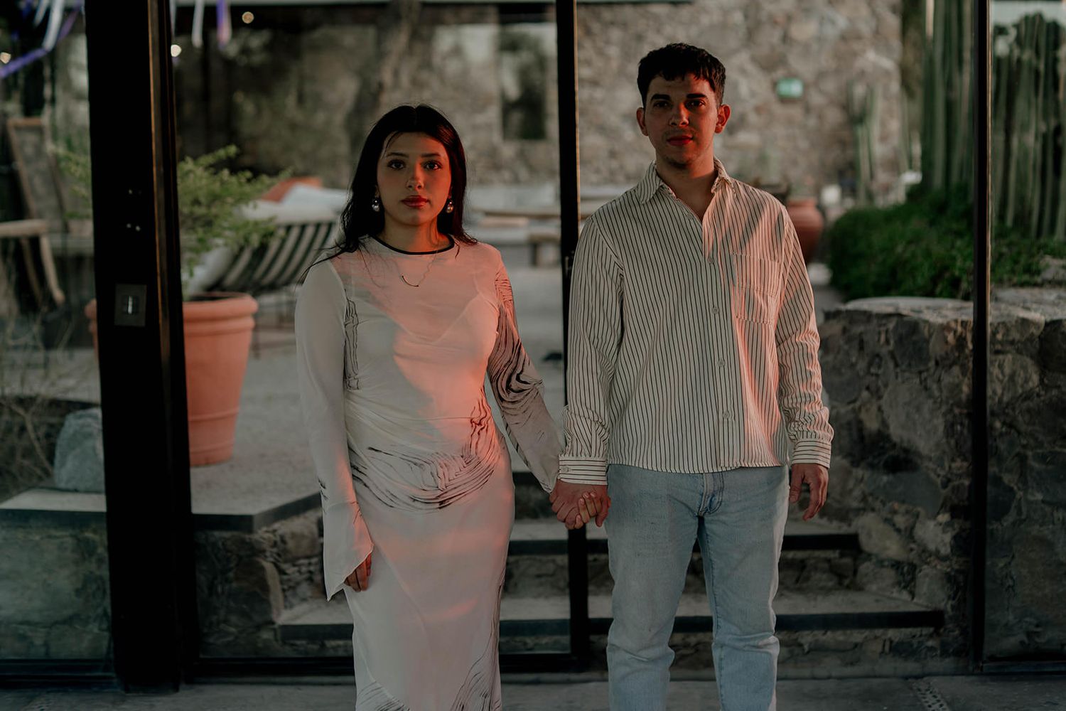 Couple in casual attire standing together in a dimly lit indoor space.