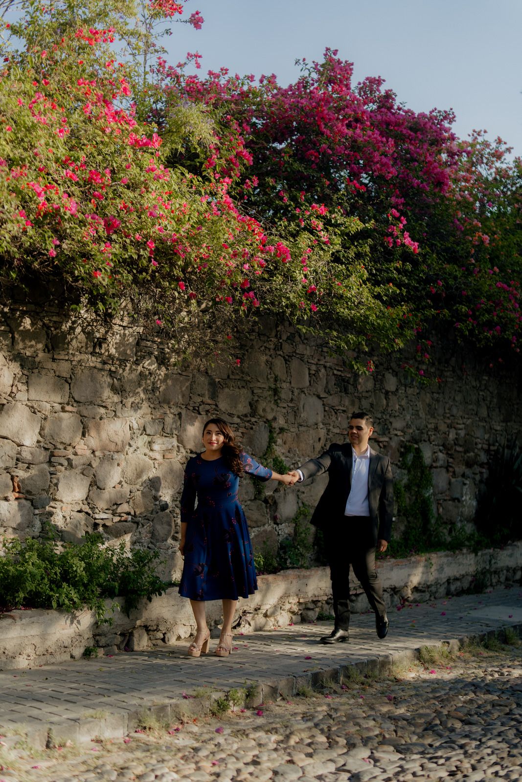 Couple dancing near stone wall covered in blooming pink bougainvillea.