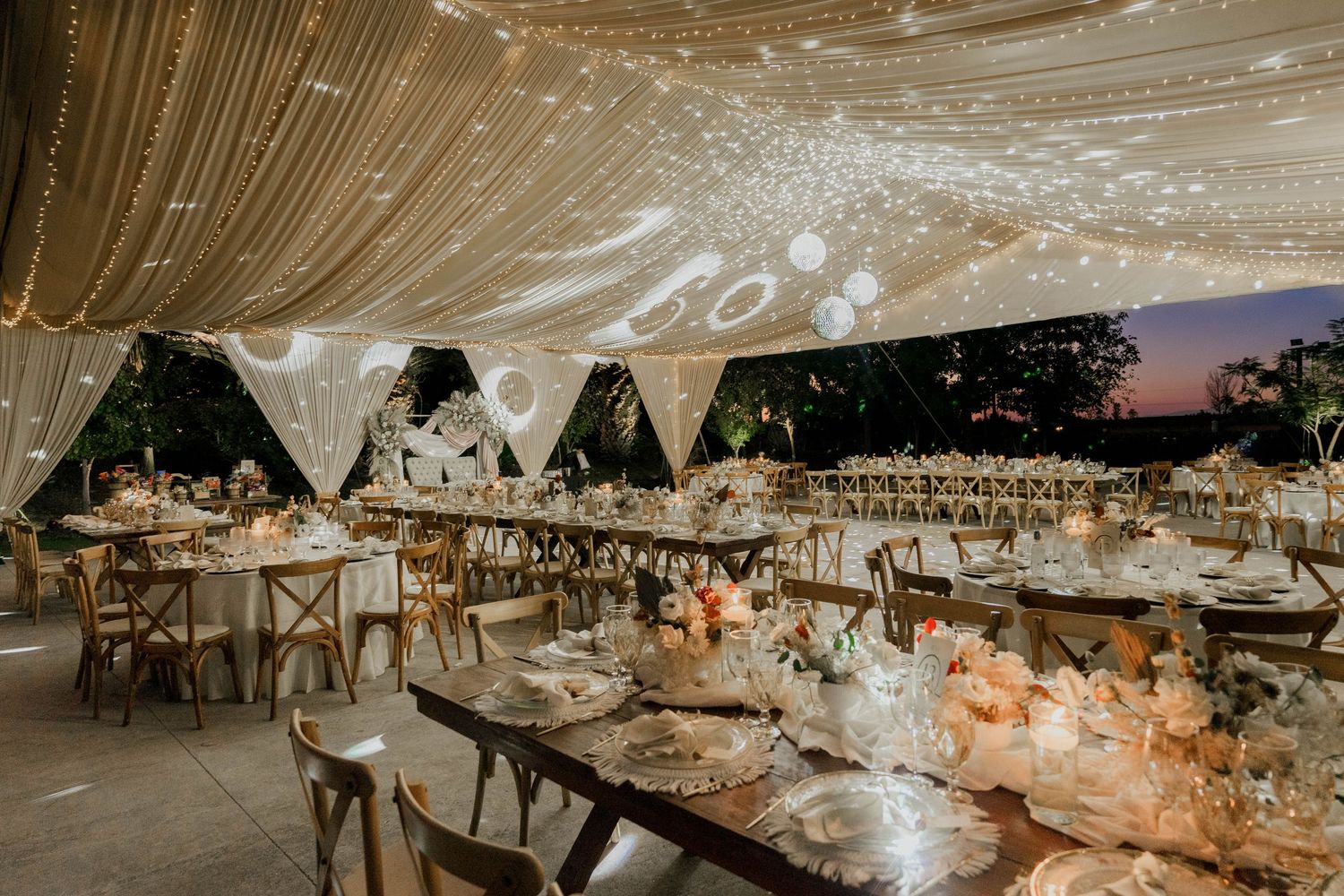 Elegant wedding reception tent with draped ceiling and string lights creates a romantic atmosphere.