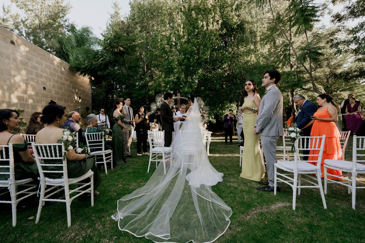 White chairs arranged in rows on a lawn for an outdoor garden wedding ceremony.