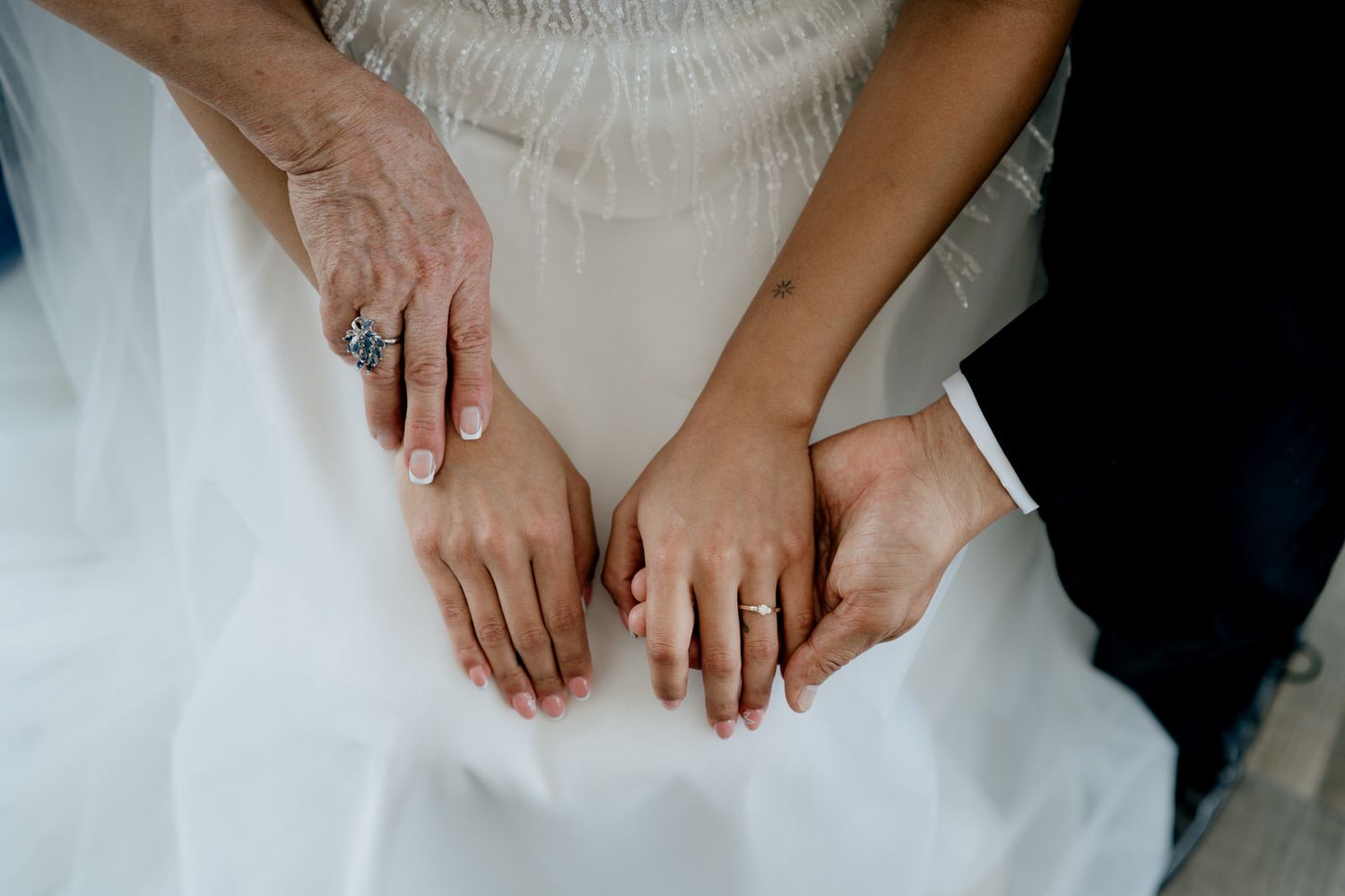 Three generations of women display wedding rings on a white bridal gown at a wedding ceremony.
