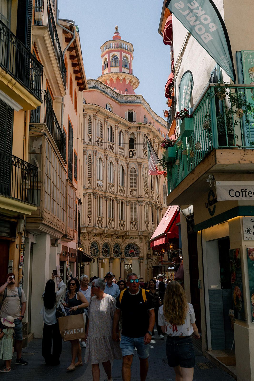 Charming European street with historic architecture and ornate domed building visible at the end of a narrow cobblestone lane.