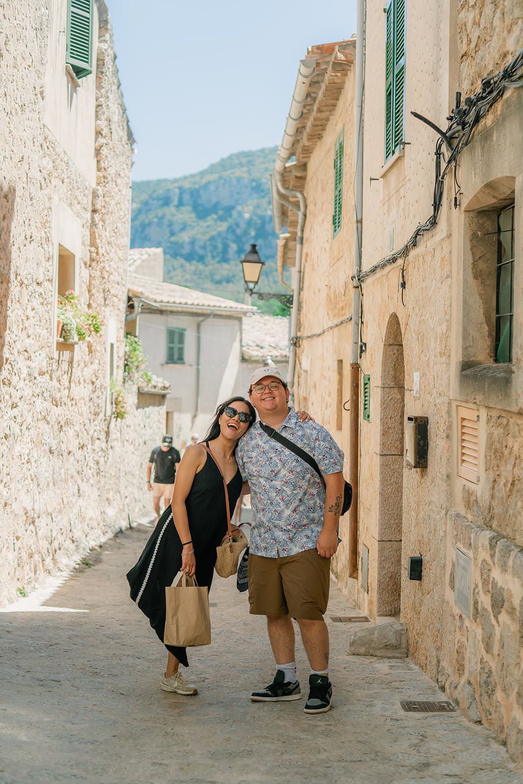 Tourists explore a charming narrow cobblestone street in a Mediterranean village with whitewashed walls and rustic architecture.