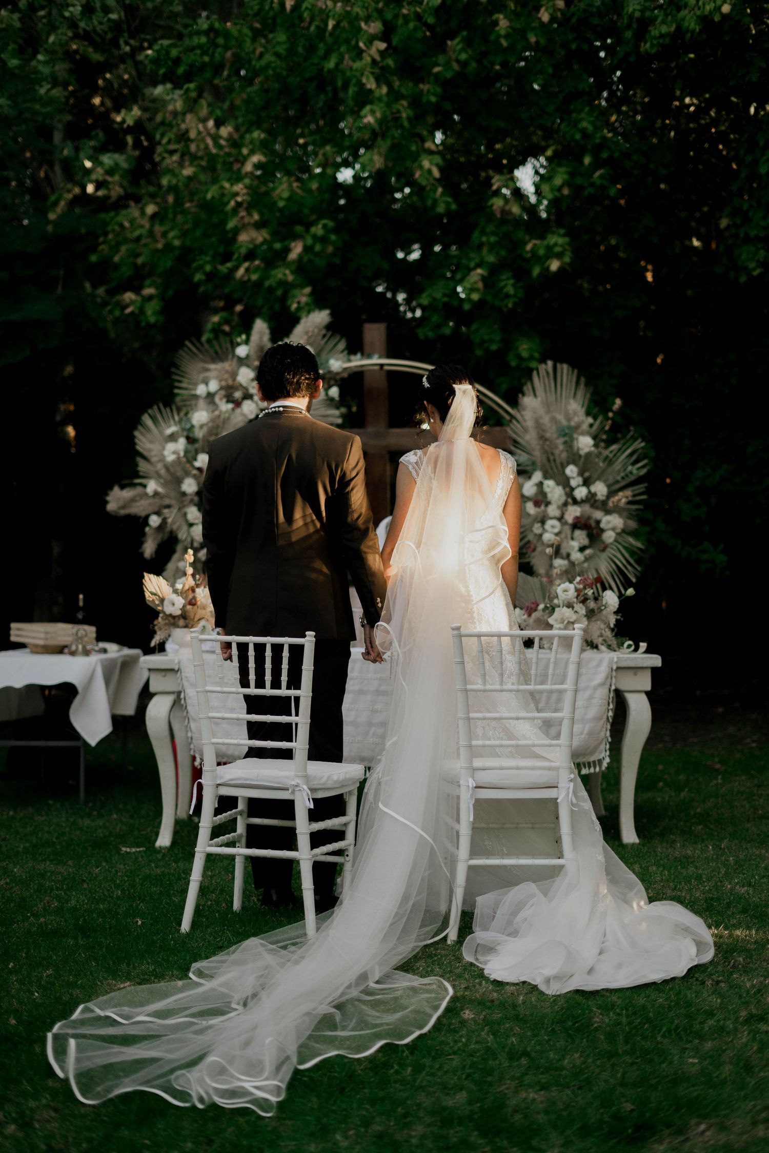 Elegant wedding scene with white chairs and flowing veils in an outdoor garden setting.