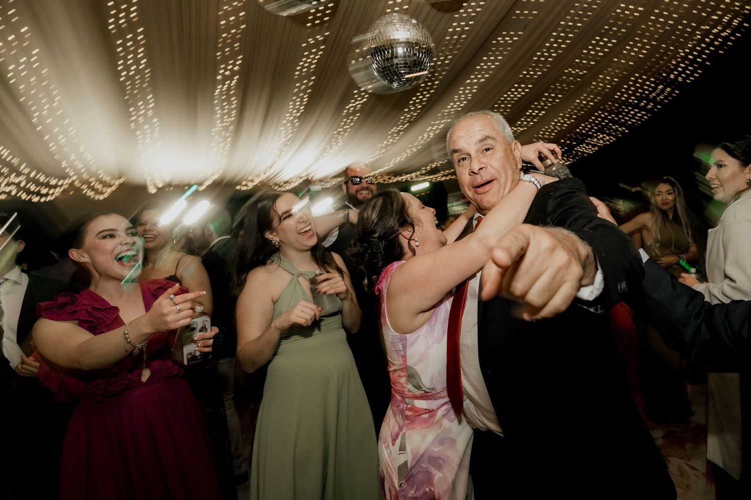Guests dancing enthusiastically under string lights at wedding reception.