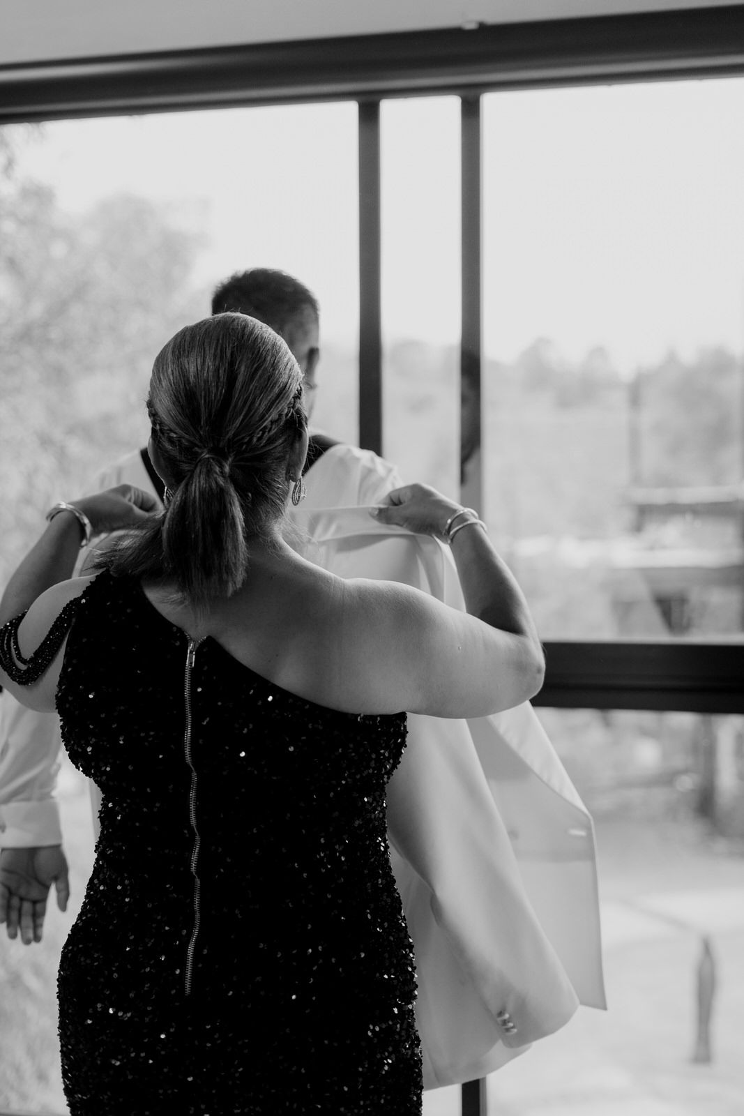 Wedding party members embrace near large windows during an emotional pre-ceremony moment.