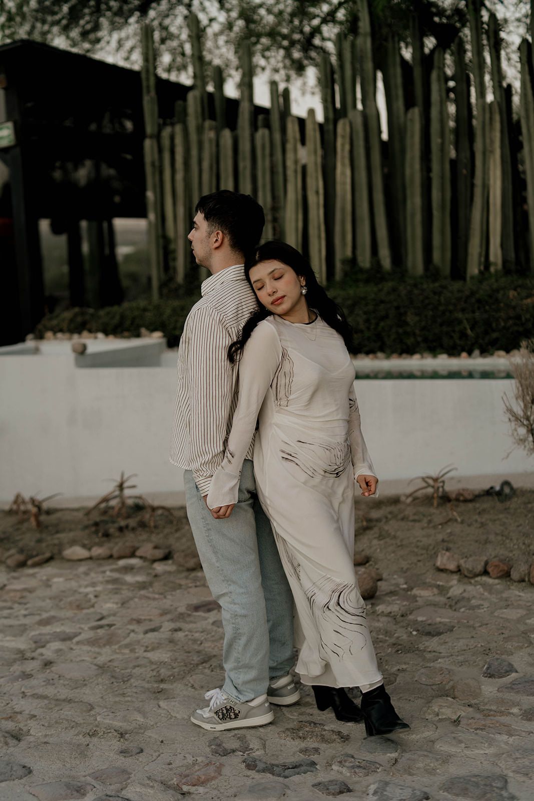 Two people dance and play together on sandy ground near a wooden fence.