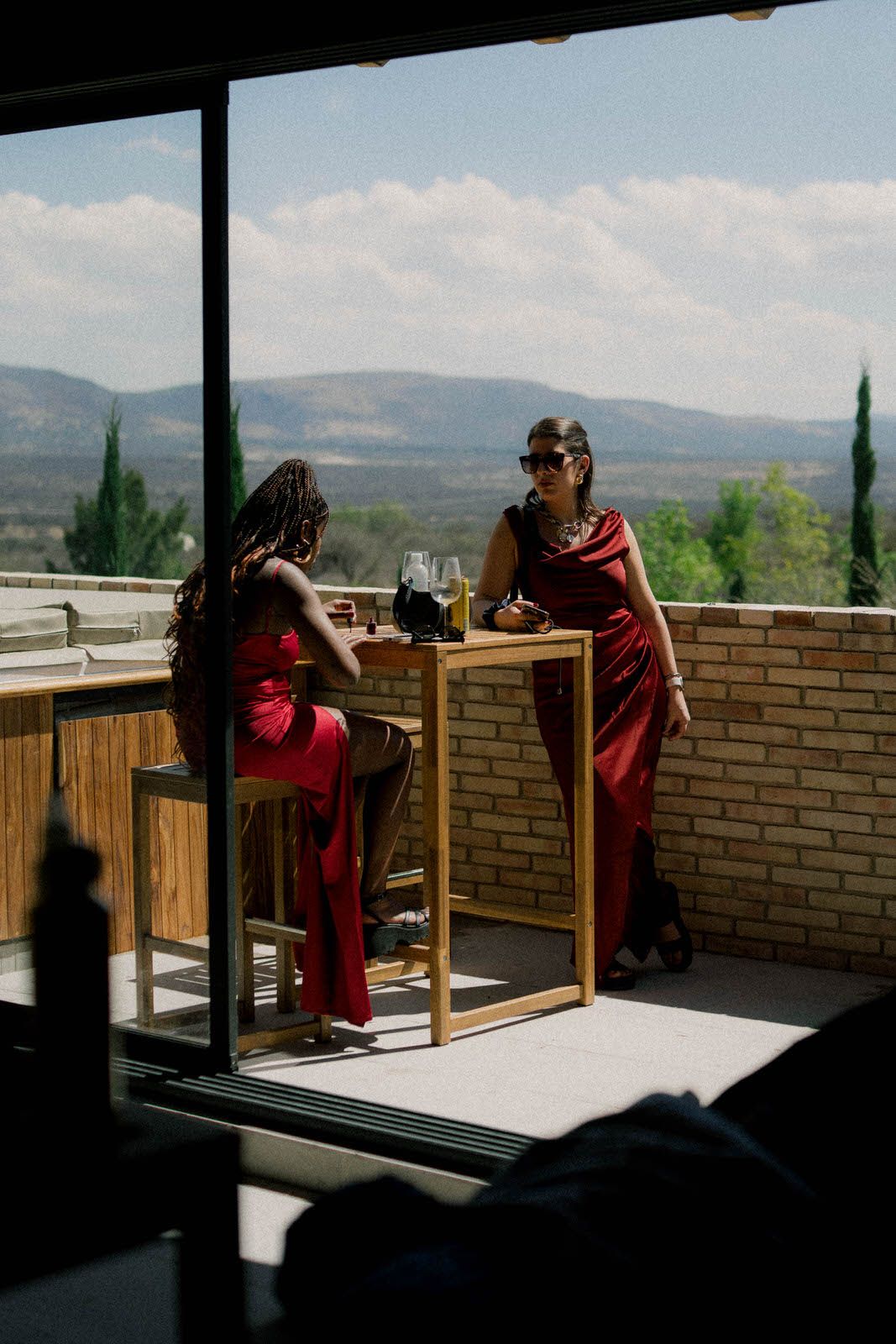 People in red attire seated at tables on a balcony overlooking mountain views.