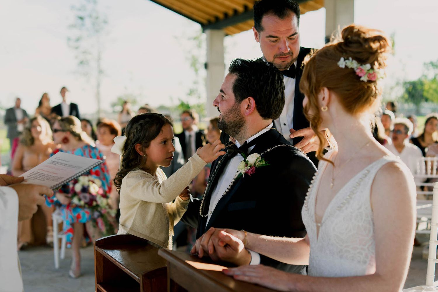 An intimate wedding ceremony moment under a covered outdoor pavilion with guests looking on.