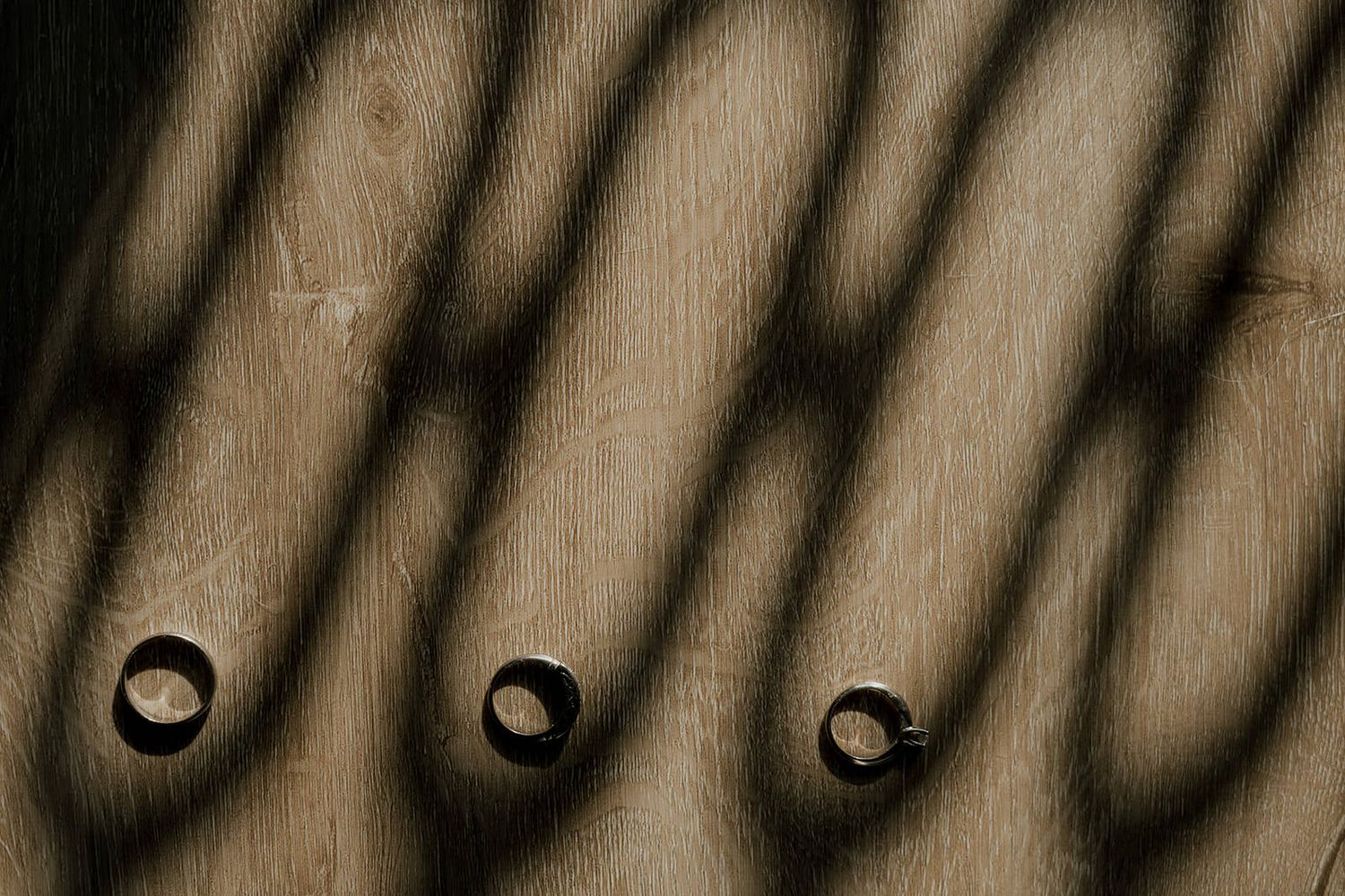 Three circular holes in wood casting diagonal shadows from sunlight filtering through a fence.