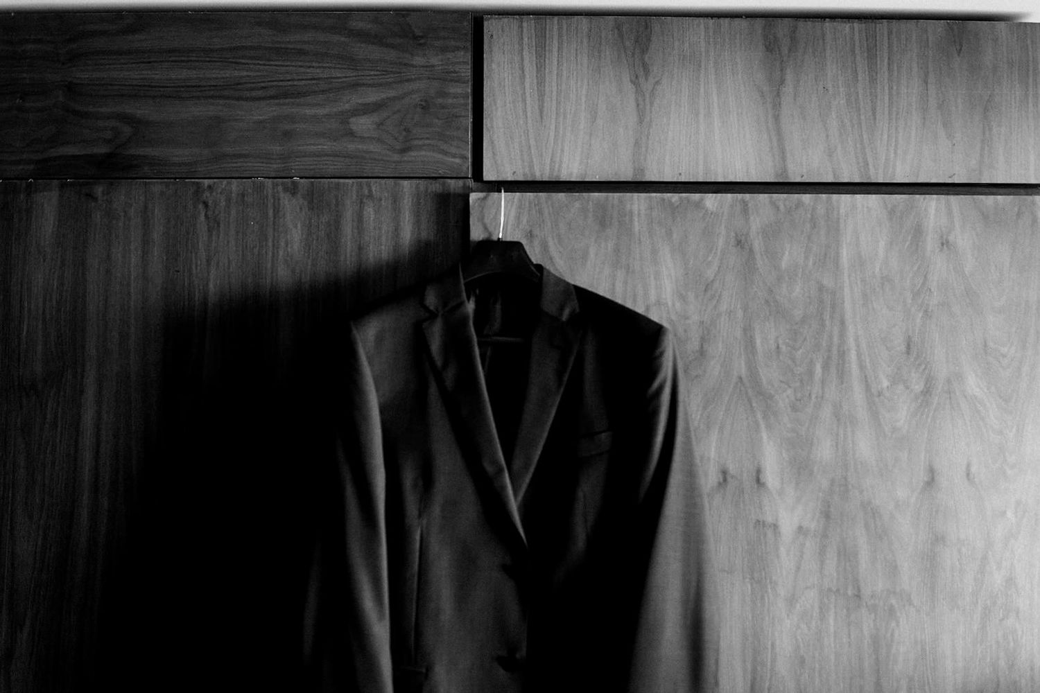 Black tuxedo jacket hanging on wooden wall in elegant black and white photography.