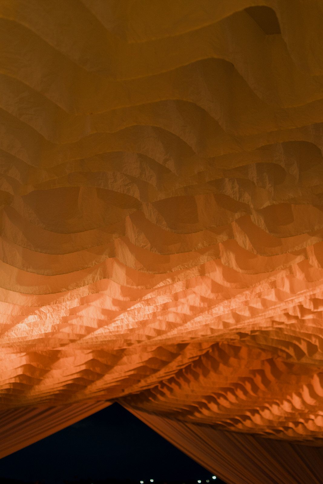 Close-up of illuminated wavy wooden ceiling architecture with warm orange tones at night.