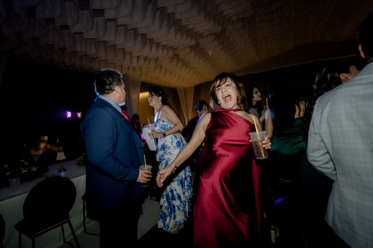 Woman in elegant red gown dances joyfully with partner at festive wedding reception celebration.