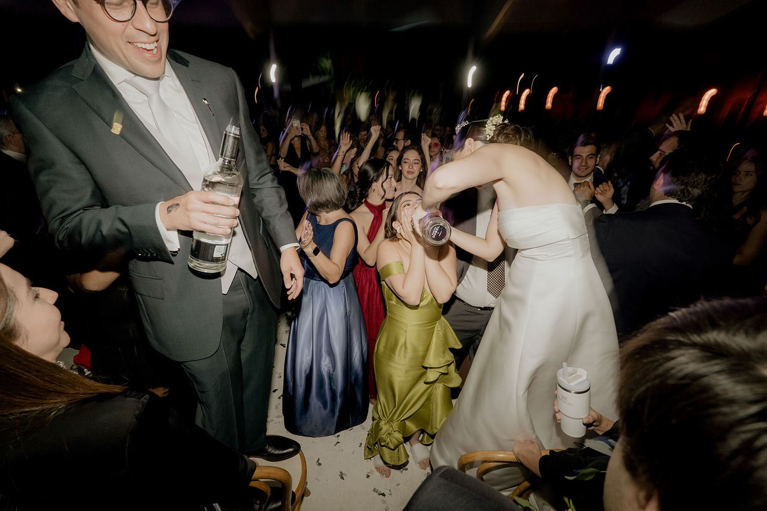 Bride and groom celebrating with champagne on the dance floor surrounded by wedding guests.