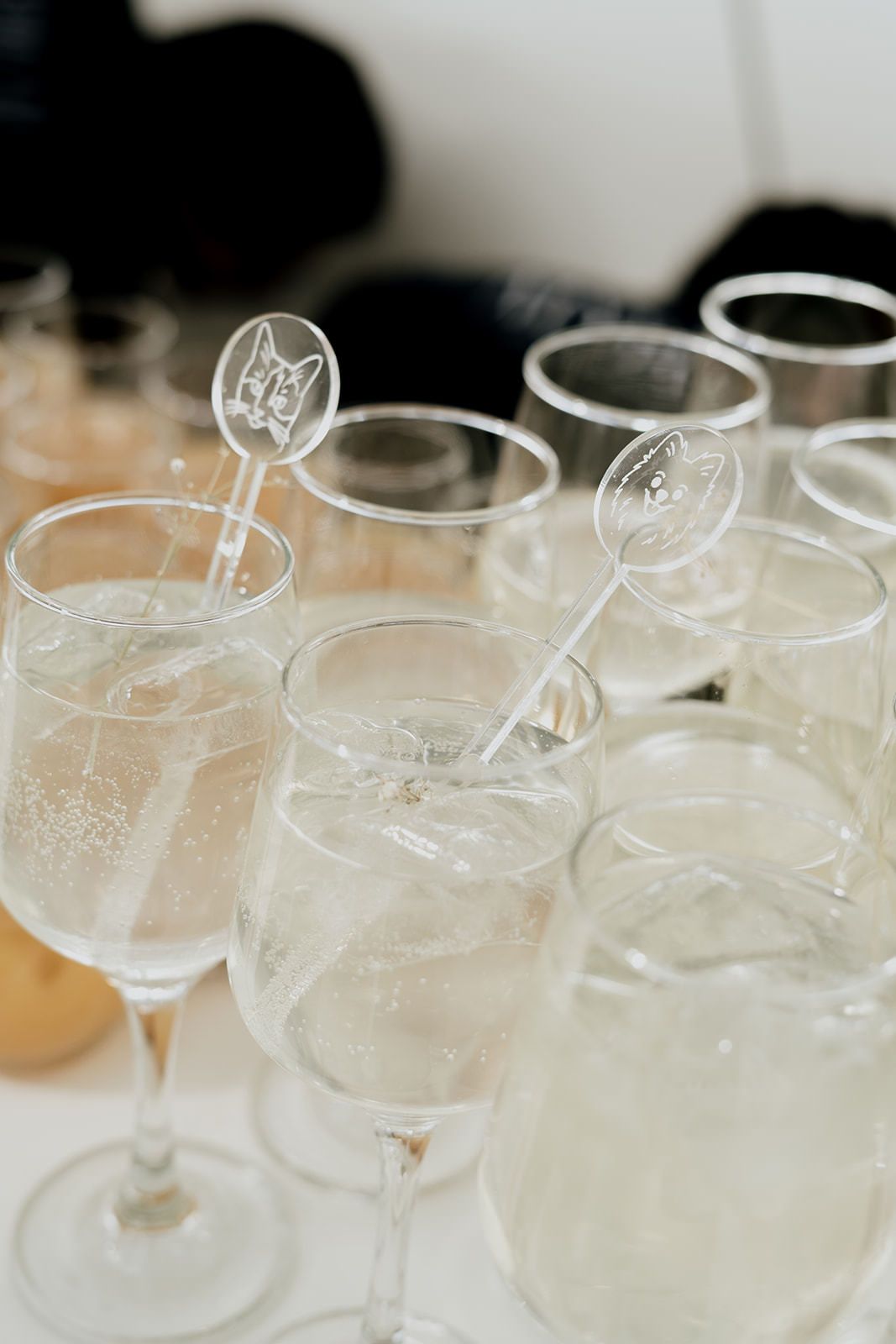 Elegant champagne flutes and cocktail glasses with decorative stirrers arranged on a white table at a wedding reception.