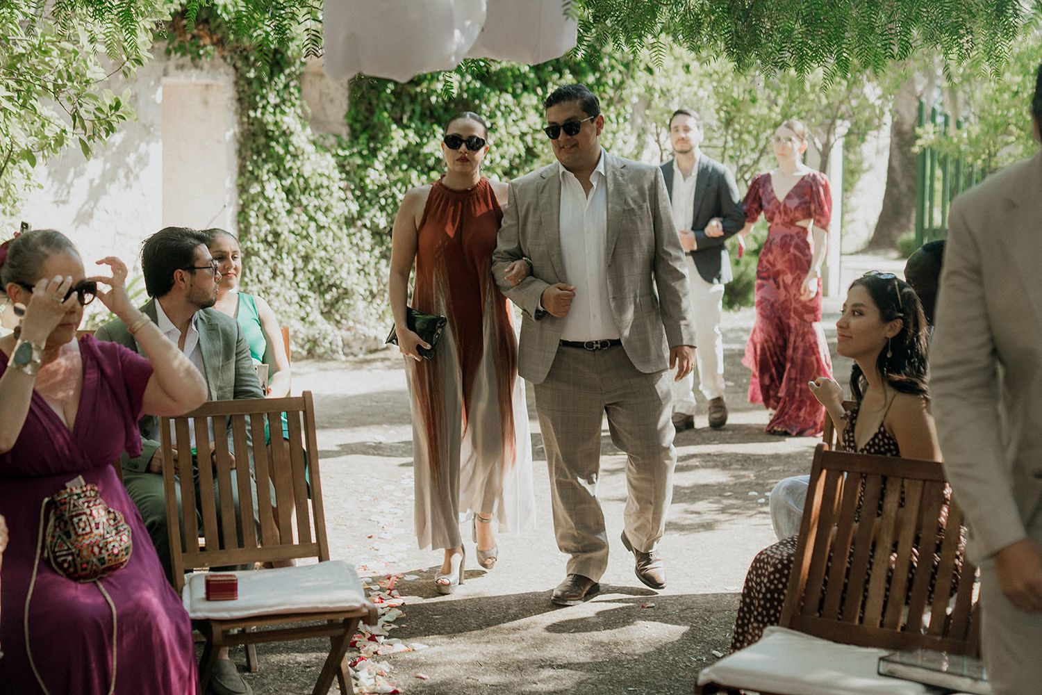 Wedding guests mingle and socialize in an outdoor garden setting under natural lighting.