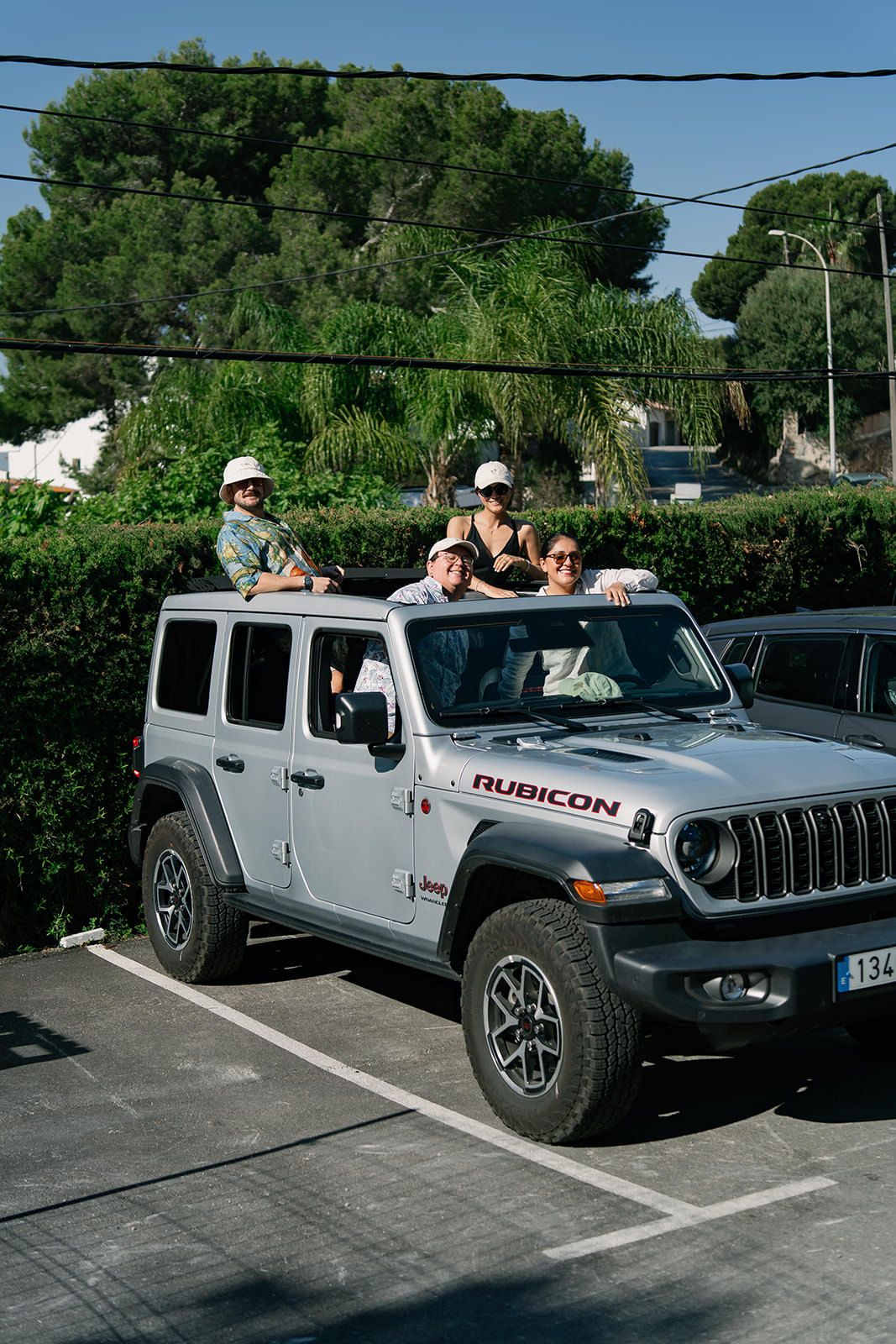 Silver Jeep Wrangler Rubicon parked outdoors with green trees and power lines in the background.