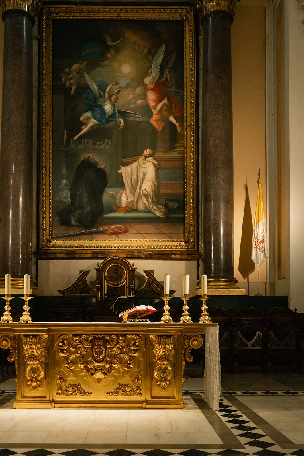 Ornate gold altar railing with decorative details in a historic church interior with classical paintings on display.