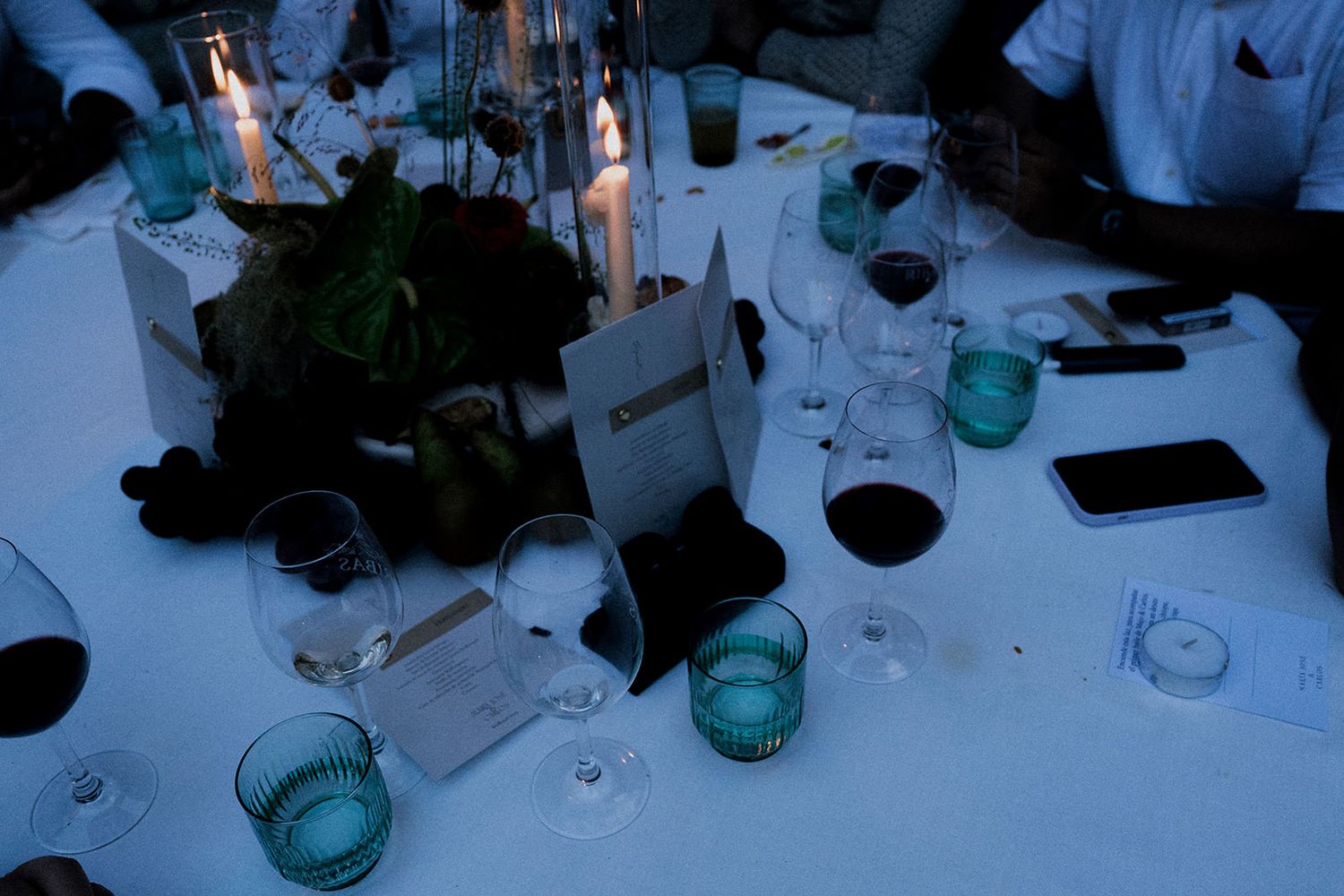 Wedding reception table settings with blue mason jars and wine glasses on white tablecloths.