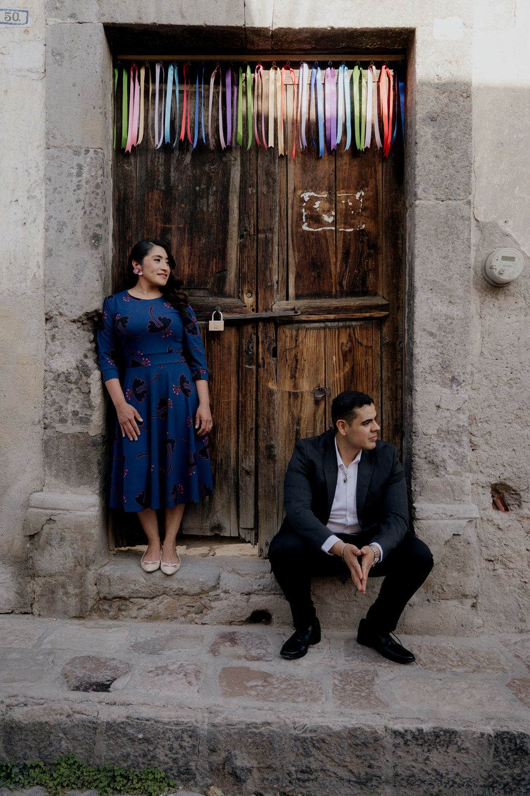 A fashionable duo poses against a weathered wooden door with rainbow ribbons above.