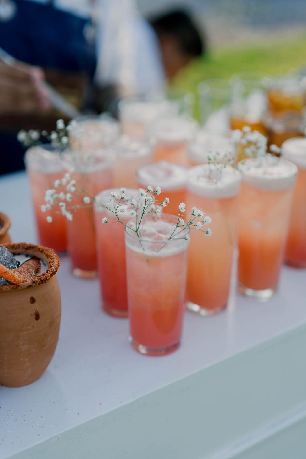 Pink cocktails garnished with baby's breath flowers lined up on a white bar counter.