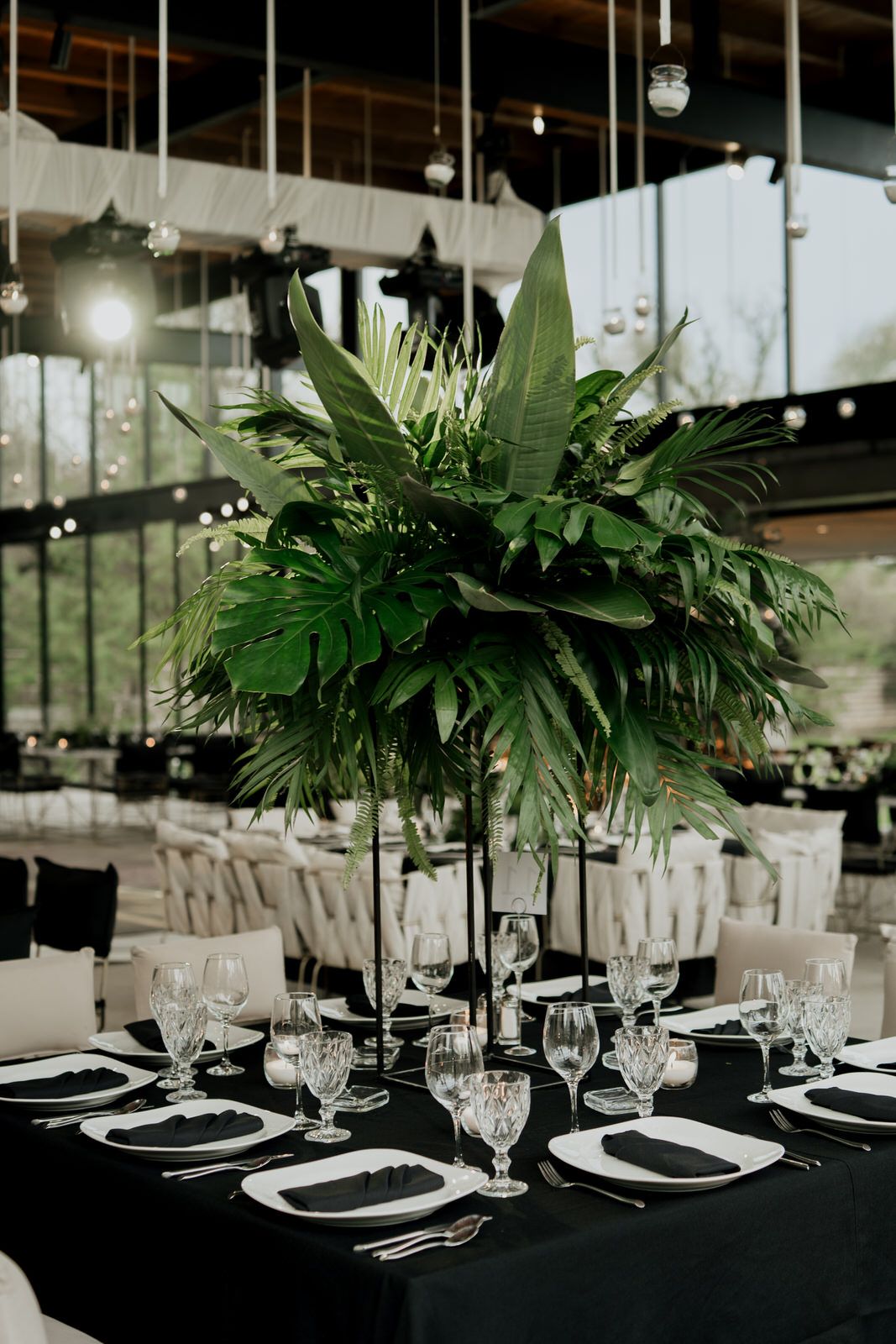 Wedding reception tables decorated with tropical greenery centerpieces and formal place settings.