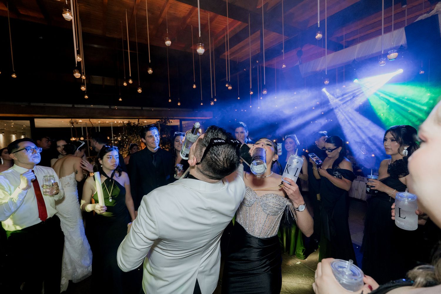 Guests dancing and celebrating under dramatic blue and green lighting at an indoor event.