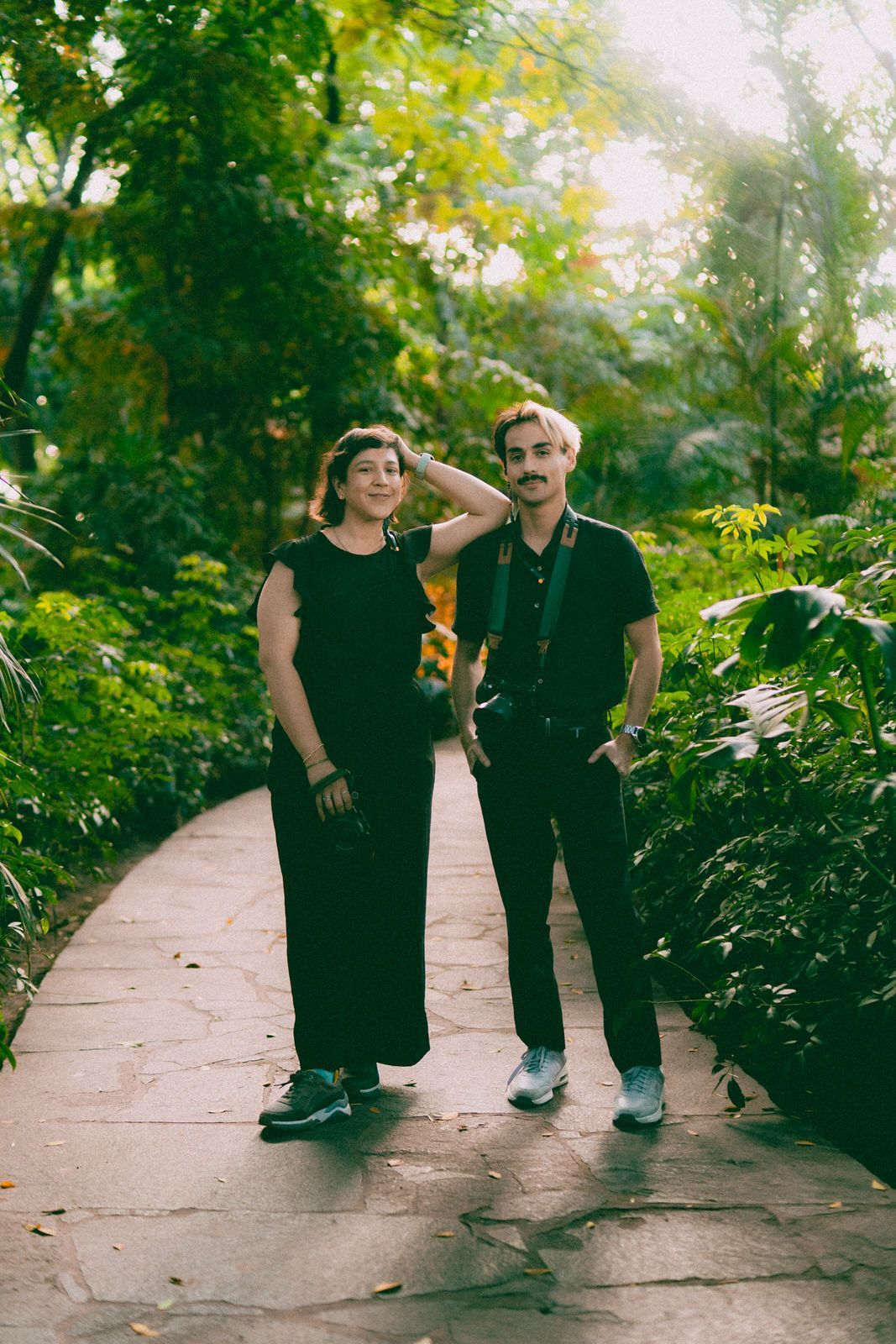 A couple walks along a stone pathway surrounded by vibrant green garden foliage.