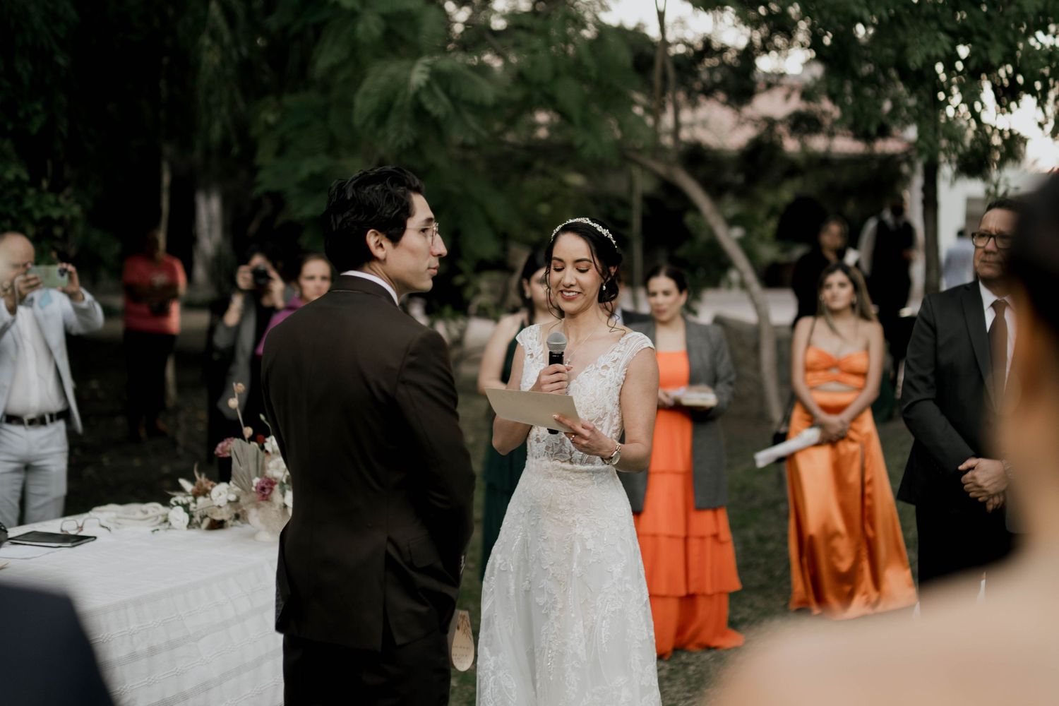 Wedding ceremony setup with bridesmaids in orange dresses standing outdoors.